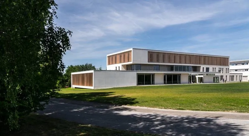 Côté sud sur la prairie, une partie du rez-de- chaussée s’étire en avant-plan, du corps vertical à R+2, dans un volume horizontal qui révèle la pente du terrain naturel et donne un socle à l’ensemble.