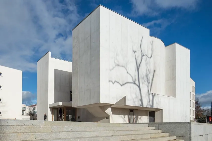 Façades sud et ouest. Très peu ouvert sur l’extérieur, l’édifice  se présente comme un ensemble de volumes imbriqués de béton blanc.
