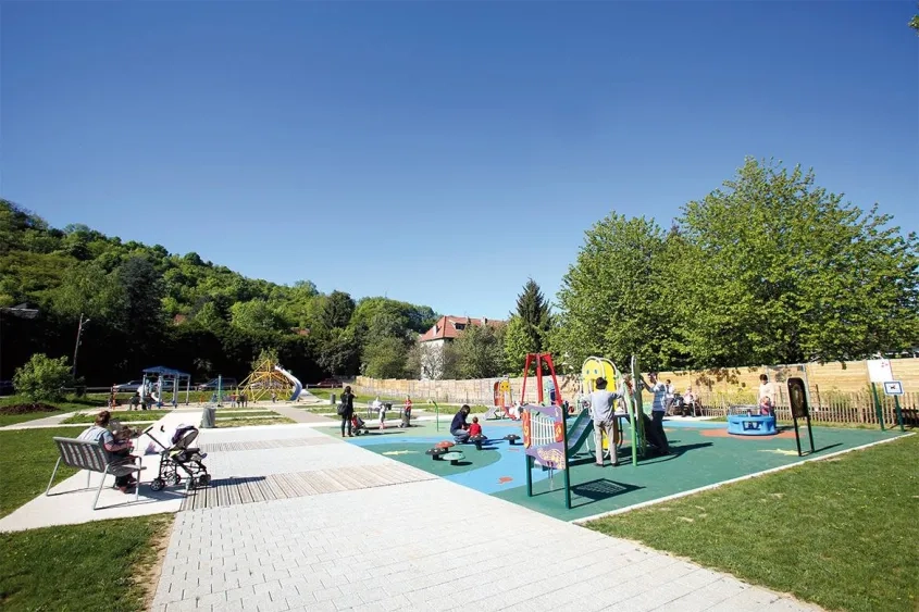 en bordure de route et du doubs, le square de Velotte (2 800 m2) compte deux aires de jeux pour enfants. ses cheminements réalisés en béton décoratif Articimo® (holcim Bétons) micro- désactivé de ton pierre s’harmonisent parfaitement avec les autres matériaux utilisés : le bois (pour le platelage) et la pierre (pour le pavage).