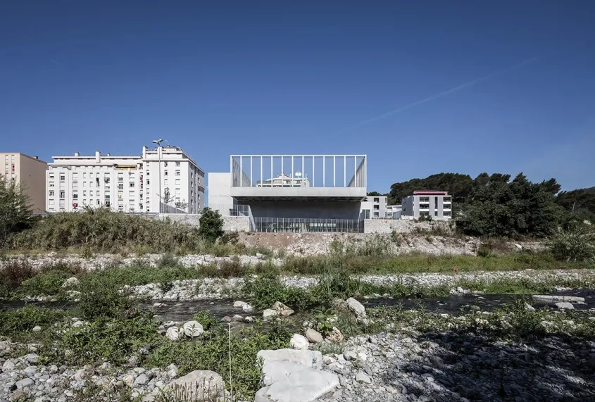 La salle s’implante perpendiculairement au fleuve et s’insère dans son contexte urbain par sa justesse et sa sobriété.