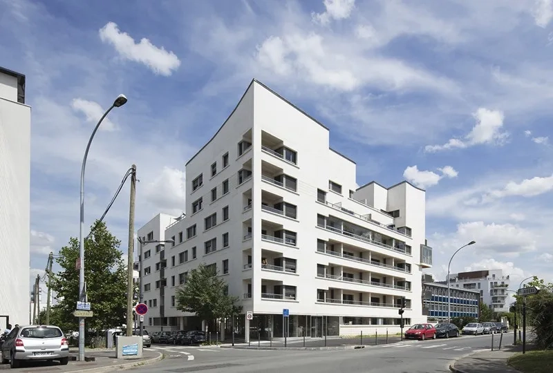 À l’angle des deux rues, où l’ouverture du hall d’accueil dessine la partie basse de l’immeuble, la pente de la toiture anime la partie haute.