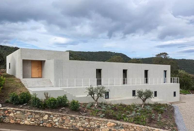 La maison se déploie par un jeu de volumes en béton sablé aménagés dans la pente. La maison se déploie par un jeu de volumes en béton sablé aménagés dans la pente.