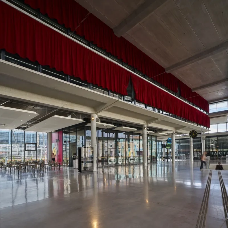 dans la continuité du hall, l’espace d’attente et d’accueil se glisse sous le premier niveau partiel de parking perceptible derrière les rideaux rouges. dans la continuité du hall, l’espace d’attente et d’accueil se glisse sous le premier niveau partiel de parking perceptible derrière les rideaux rouges.