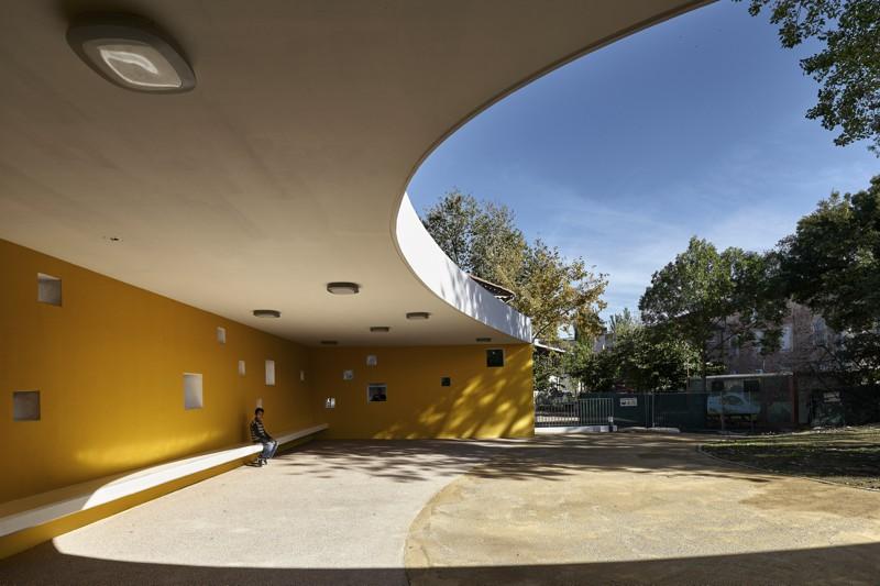 Les percements carrés dans le mur jaune du préau offrent des vues cadrées sur les espaces alentour.