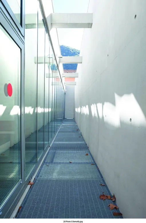 espace aménagé entre les grandes baies vitrées de la salle d’audience pénale et la paroi de façade en béton blanc sur laquelle se réfléchit la lumière naturelle.