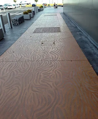 Le béton brun-rouge renvoie à la couleur de l’entrée en imitation Corten. Il a été traité grâce à des pochoirs et à un sablage de la surface « pour ne pas marquer le sol en profondeur ». Le béton brun-rouge renvoie à la couleur de l’entrée en imitation Corten. Il a été traité grâce à des pochoirs et à un sablage de la surface « pour ne pas marquer le sol en profondeur ».