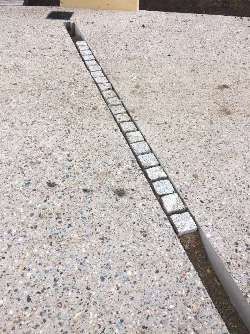 Particularité des bandes structurantes en pavés : prévues pour recevoir de la terre et être engazonnées, elles ont été réalisées dans des réservations créées dans le béton, au moment du coulage. Particularité des bandes structurantes en pavés : prévues pour recevoir de la terre et être engazonnées, elles ont été réalisées dans des réservations créées dans le béton, au moment du coulage.