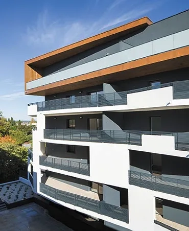 Façade principale du bâtiment haut avec ses grandes loggias orientées sud- ouest dont les rives en béton peint en blanc soulignent le déploiement. Façade principale du bâtiment haut avec ses grandes loggias orientées sud- ouest dont les rives en béton peint en blanc soulignent le déploiement.