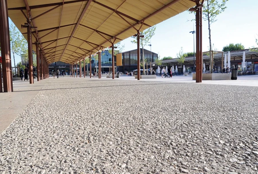 Sous la halle couverte, le béton de granulométrie 20/40 accentue l’aspect minéral de la place. Halle couverte