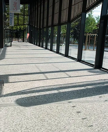 La coursive en béton bouchardé prolonge le parvis à l’intérieur du bâtiment. La coursive en béton bouchardé prolonge le parvis à l’intérieur du bâtiment.