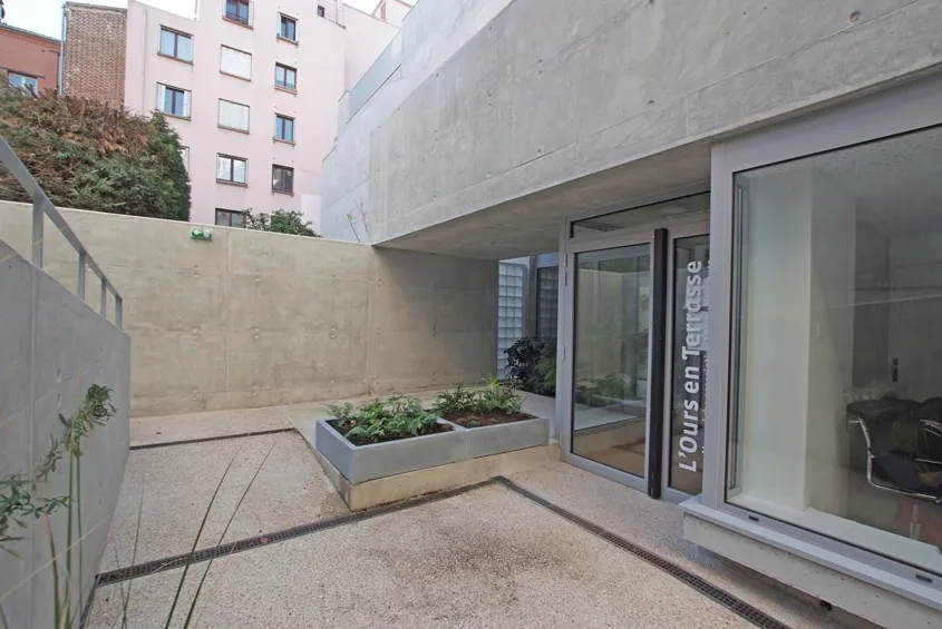 Le garde-corps de la terrasse extérieure du premier étage cadre le creux dans lequel est aménagée l’entrée de la crèche.