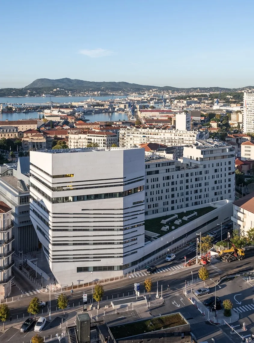 Volumétriquement, le bâtiment est composé d’un socle et d’un plot qui s’élève pour aller chercher la vue. Une alternance de pleins et de vides découpe la façade en lanières, comme un prisme sculpté dans la masse. Volumétriquement, le bâtiment est composé d’un socle et d’un plot qui s’élève pour aller chercher la vue. Une alternance de pleins et de vides découpe la façade en lanières, comme un prisme sculpté dans la masse.