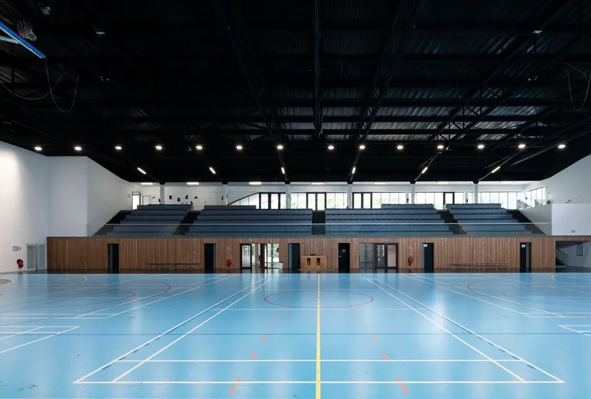Gymnase – Une nappe structurelle faite de six poutres métalliques en treillis, peintes en noir, permet de franchir les 45 m de portée libre.