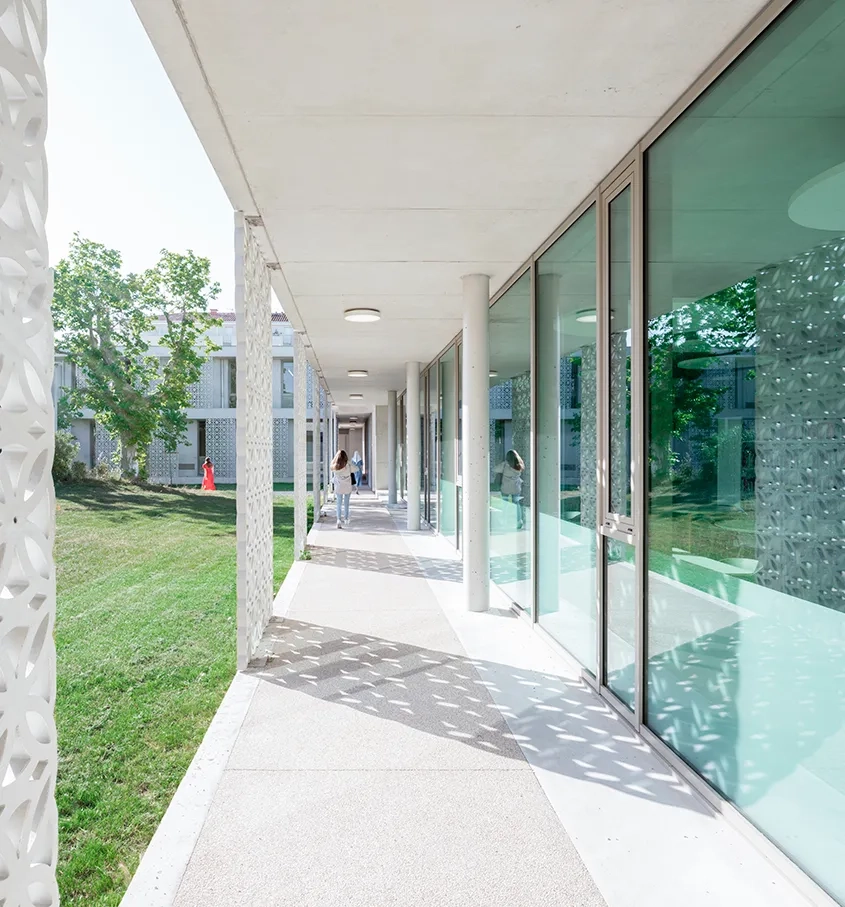 Les différents bâtiments de l’institution sont desservis par des coursives extérieures. Celles-ci sont bordées et ponctuées par les mêmes éléments de panneaux de façade ajourés en béton fibré.