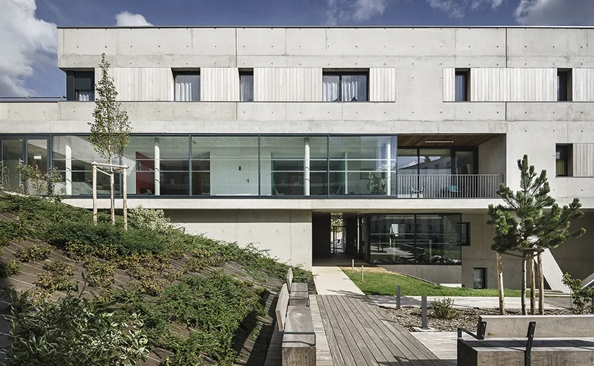 Façade ouest sur l’intérieur de l’îlot. La partie en béton brut abrite les appartements et la façade vitrée le cabinet médical.