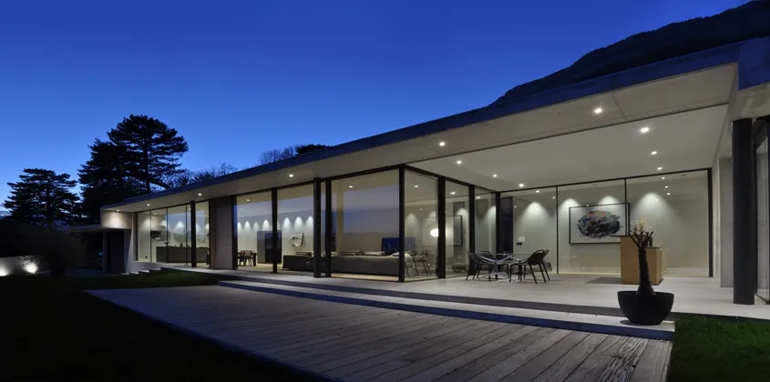 En soirée, l'éclairage artificiel met en valeur l'intérieur devancé par la loggia et le platelage en bois de la terrasse. Le béton n'est dès lors plus visible qu'au sol.