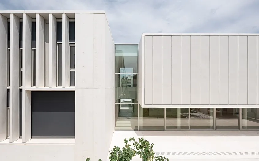 L’édifice se fragmente en belles volumétries de béton blanc tenues par de grandes failles vitrées qui ménagent des transparences d’est en ouest.