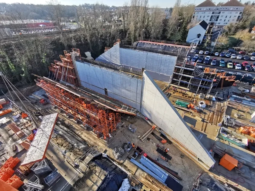 Le pont-rail a été construit à 49 mètres de son futur emplacement, au milieu du parking d’Épinay-sur-Orge. L’ouvrage en béton armé est constitué d’un cadre rectangulaire (au centre de la photo), complété de deux travées d’approche reposant sur des bracons inclinés à 45°. Quatre murs en ailes (l’un d’eux est visible en bas à droite) viennent compléter l’ouvrage.