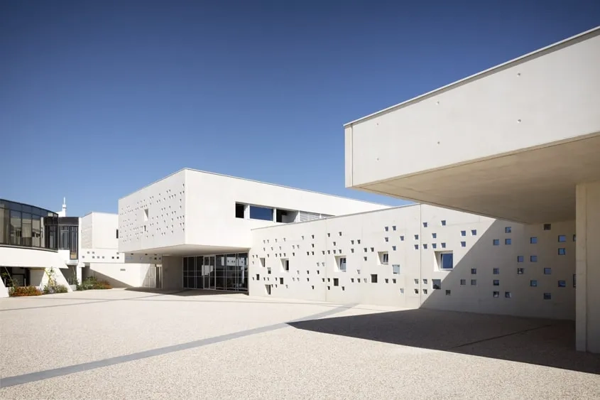 La façade principale en béton blanc est animée par un ensemble de perforations carrées, réparties de façon aléatoire.