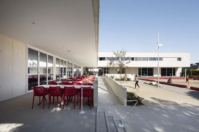 La forme en équerre cadre les espaces sportifs extérieurs constitués par le terrain de beach-volley et le city-stade, sur lesquels donnent des terrasses des pôles restauration et animation.