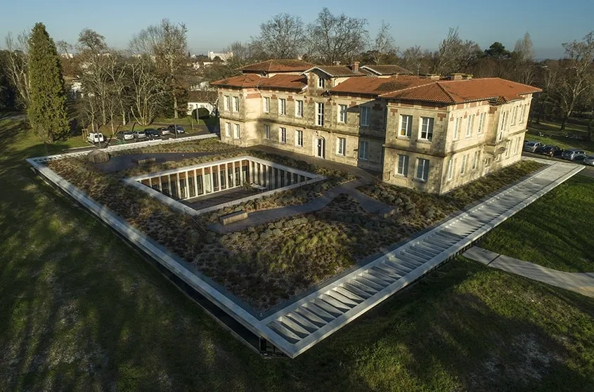 Avec sa toiture végétalisée, l’extension semi-enterrée se fond dans le parc paysager.