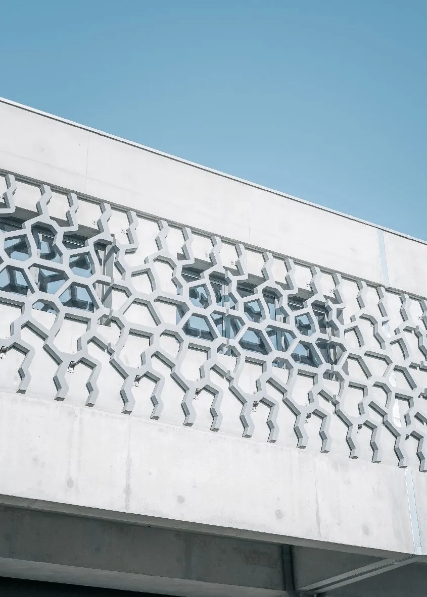Le motif de la résille en panneaux préfabriqués de béton fibré à ultra hautes performances (BFUP) disposée au premier étage de la façade principale (est) est inspiré par l’empreinte de pneu d’un engin routier, comme un clin d’œil à la fonction de l’équipement. Le motif de la résille en panneaux préfabriqués de béton fibré à ultra hautes performances (BFUP) disposée au premier étage de la façade principale (est) est inspiré par l’empreinte de pneu d’un engin routier, comme un clin d’œil à la fonction de l’équipement.