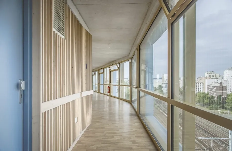 Placé le long de la façade ouest à chaque étage de la résidence, le couloir de distribution des studios offre un espace intermédiaire lumineux, ouvert sur le paysage environnant. Placé le long de la façade ouest à chaque étage de la résidence, le couloir de distribution des studios offre un espace intermédiaire lumineux, ouvert sur le paysage environnant.