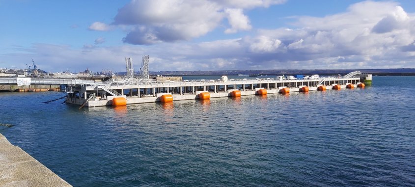 Vue générale du ponton flottant, de la passerelle métallique de liaison au quai (à gauche) et du musoir (à droite), qui constitue le point fixe d’accostage et d’amarrage des frégates côté mer. 