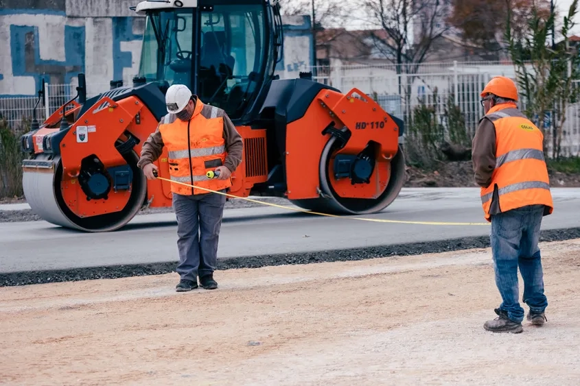Pendant que la première couche de la première bande de BCR est compactée par un VT2, l’entreprise effectue les mesures pour positionner une nouvelle bande en respectant le plan de bétonnage en peigne. (© Béton Vicat)