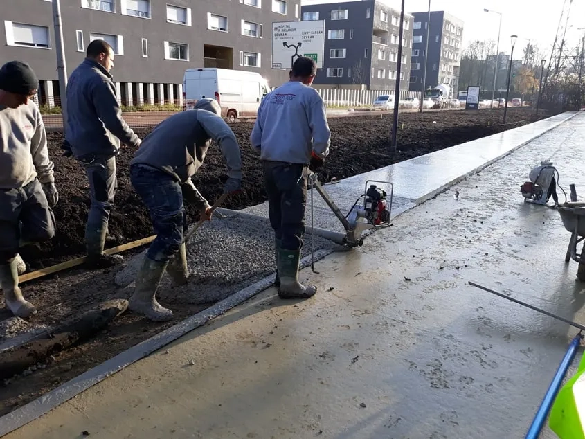 Le tirage du béton au rouleau Striker. Il n’a pas été vibré pour ne pas faire descendre le granulat, qui doit rester en surface pour le bon aspect visuel de la finition piqué. Le tirage du béton au rouleau Striker. Il n’a pas été vibré pour ne pas faire descendre le granulat, qui doit rester en surface pour le bon aspect visuel de la finition piqué.