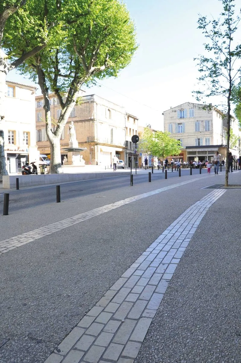 Les cours ont reçu un revêtement de béton désactivé avec des cailloux concassés clairs et un calepinage de bandes structurantes en pierres calcaires naturelles Cénia. Les cours ont reçu un revêtement de béton désactivé avec des cailloux concassés clairs et un calepinage de bandes structurantes en pierres calcaires naturelles Cénia.